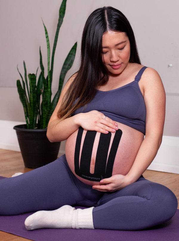 pregnant woman doing yoga with baby belly supported by black kinesiology tape